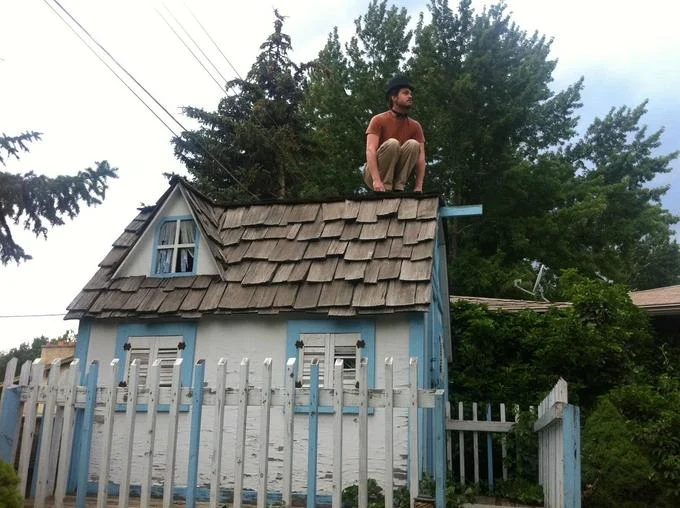 Owling — Man crouched on the peak of a shed roof imitating an owl