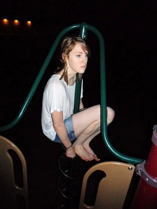 Woman crouched on top of a playground spring rider at night, owling