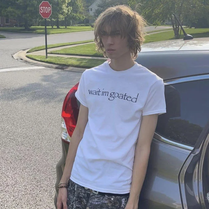 Papyrus Irony — Person wearing 'wait im goated' Papyrus font t-shirt in suburban setting
