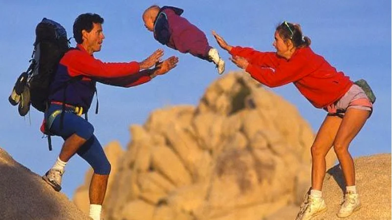 Parents Throwing Baby — Two hikers in red jackets tossing a baby between rocks