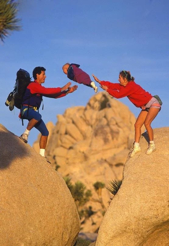 Portrait framing of parents throwing baby between two boulders