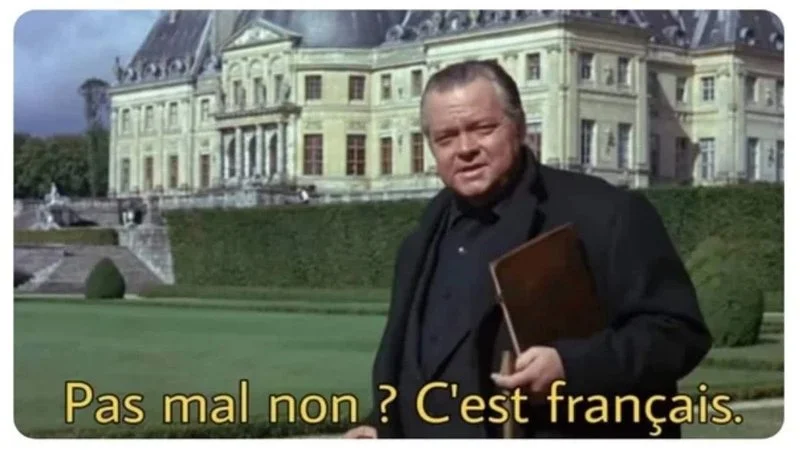 Pas Mal Non Cest Francais — A screenshot from La Classe Américaine showing Orson Welles standing on the Vaux-le-Vicomte château lawn with the subtitle 'Pas mal