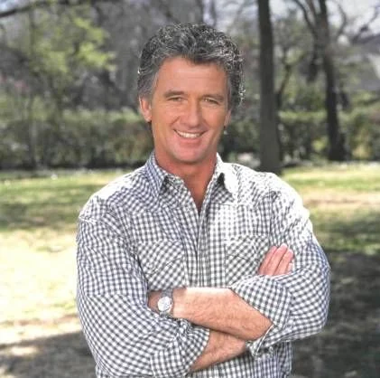 Patrick Duffy smiling in a checkered shirt with arms crossed outdoors