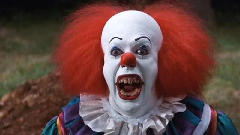 Tim Curry as Pennywise the Clown grinning menacingly with rotten teeth