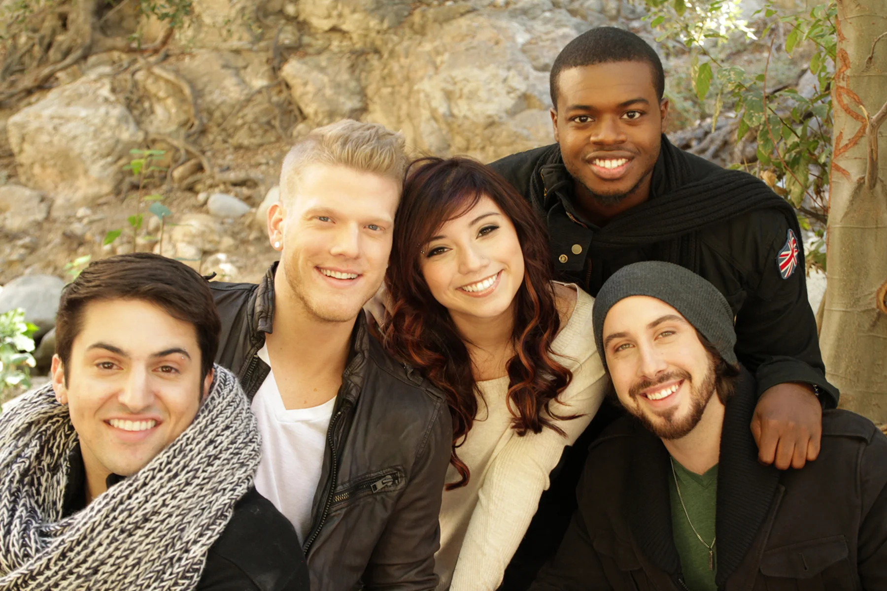 Five members of Pentatonix smiling in a professional group photo outdoors