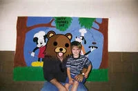 Photoshop Request Threads — A family posed in front of a cartoon theme park backdrop with an alternative facial edit applied to one member.