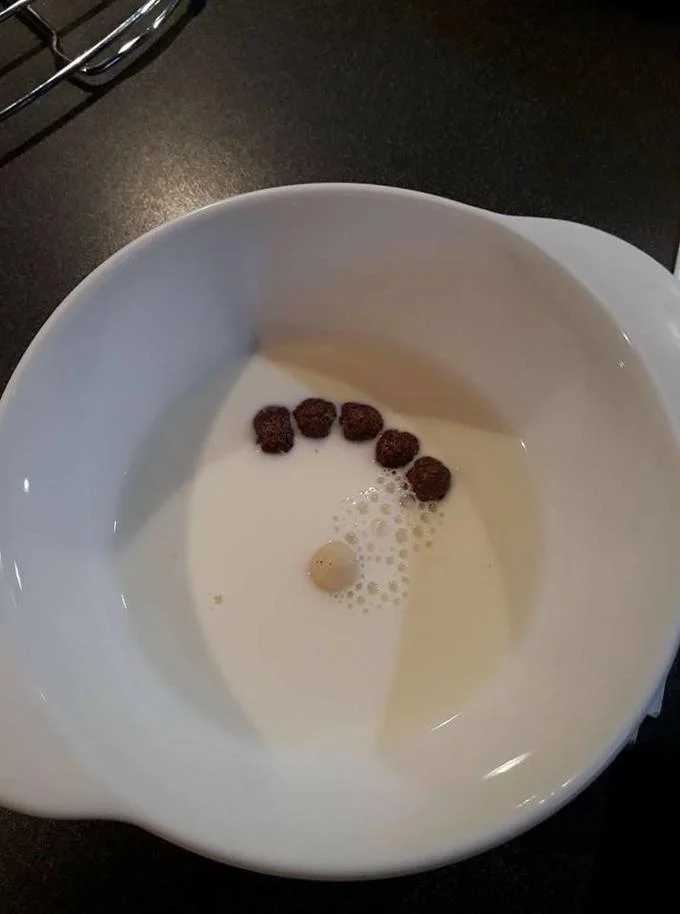 Piper Perri Surrounded — White bowl of milk with five chocolate cereal balls arranged around one small pale piece, mimicking the meme layout.