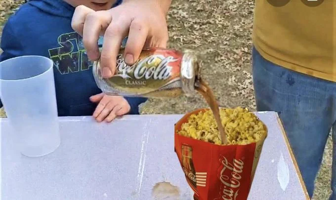 Pissy Shitties — Child pouring Coca-Cola from a can into a bag of popcorn outdoors.