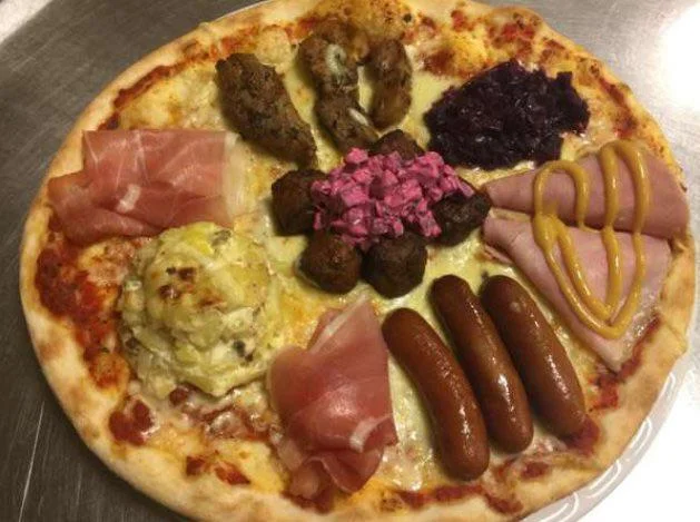 Pizza Crimes — A pizza arranged with an eccentric charcuterie-board style selection of meats including prosciutto and sausages in distinct sections.