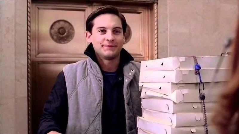 Pizza Time — Tobey Maguire as Peter Parker smiling while holding a stack of pizza boxes at a doorway.