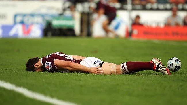 A professional rugby player lies face-down horizontally on the grass field in perfect planking position during a match.