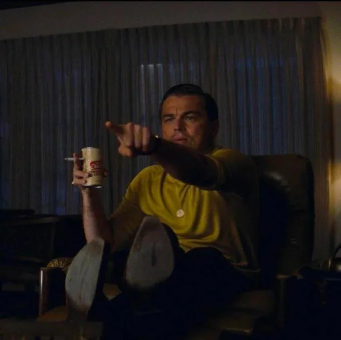 Pointing Rick Dalton — A clean text-free square crop of Leonardo DiCaprio as Rick Dalton seated in a dark leather chair pointing at the viewer.