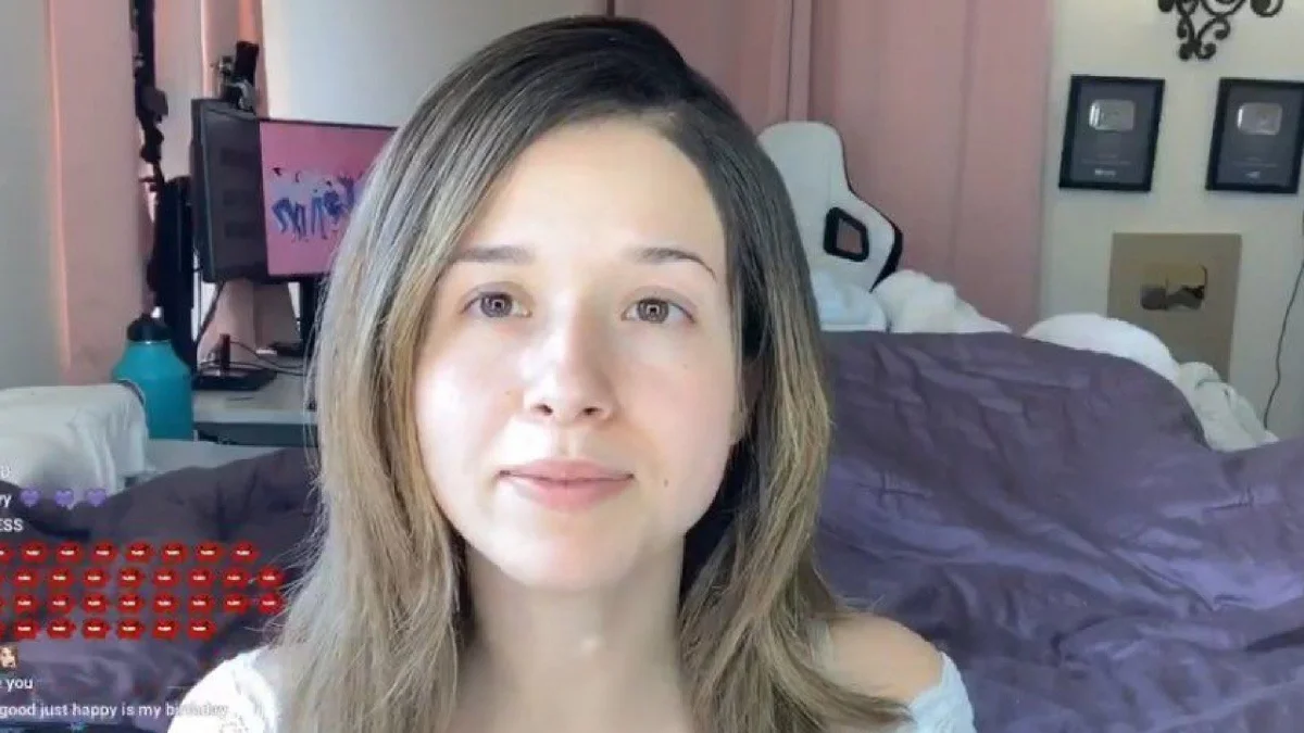 Pokimane No Makeup — Pokimane on Twitch stream without makeup, seated in her bedroom with pink walls and purple bedding