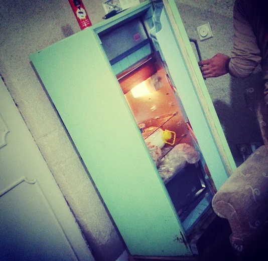 Poor Kids Of Tehran — A dim Instagram-filtered photograph of an old battered teal refrigerator being opened to reveal sparse contents inside.