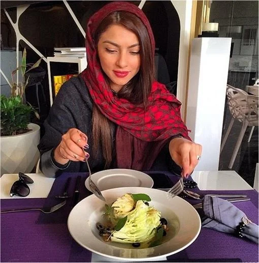 Poor Kids Of Tehran — A young Iranian woman in red hijab at an upscale restaurant with gourmet salad and designer accessories visible.