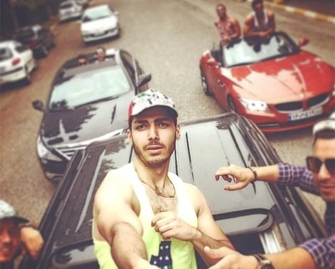 Poor Kids Of Tehran — A shirtless young Iranian man posing atop a luxury sports car with additional convertibles and wealthy figures visible behind.