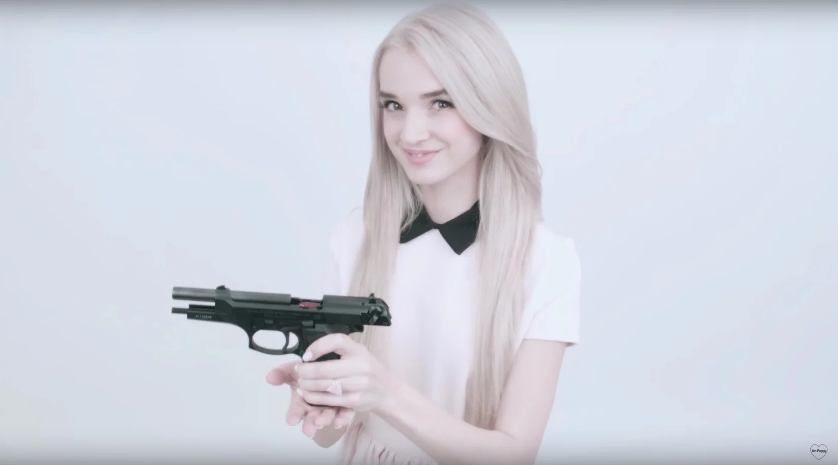 Poppy smiling while holding a black handgun in a YouTube video still