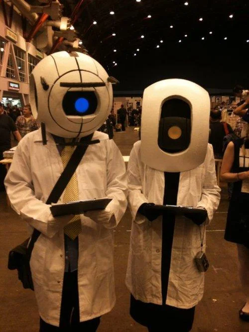 Two cosplayers dressed as Portal personality core scientists in lab coats and sphere helmets
