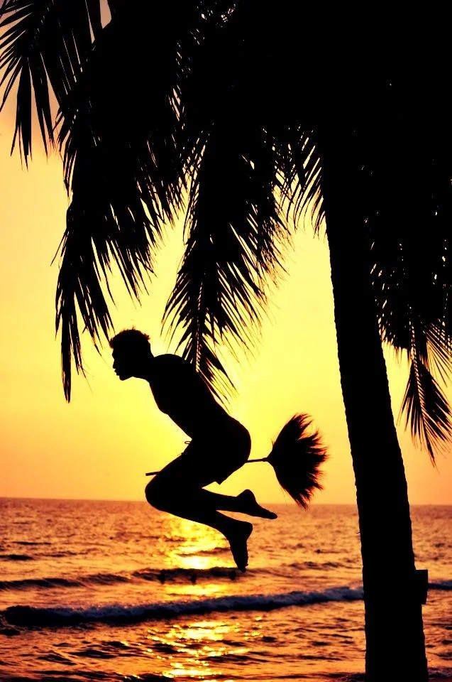 Vertical silhouette of a person pottering on a broomstick at a beach sunset