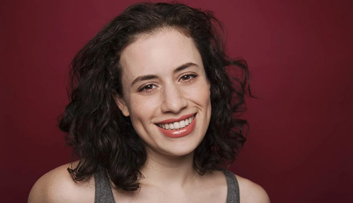 "Praxis" Girl — Headshot of smiling young woman with curly dark hair against red background