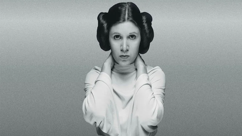 Carrie Fisher as Princess Leia in a white robe with side hair buns, black and white tribute portrait.