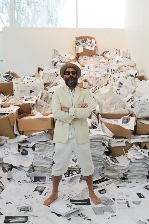 Kenneth Goldsmith standing in front of piles of printed internet pages at his Printing Out the Internet exhibition