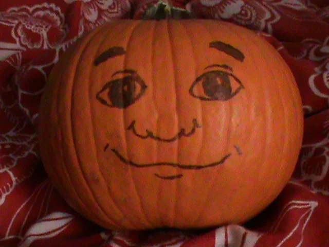Real orange pumpkin with Pumkin character face drawn in marker on red cloth