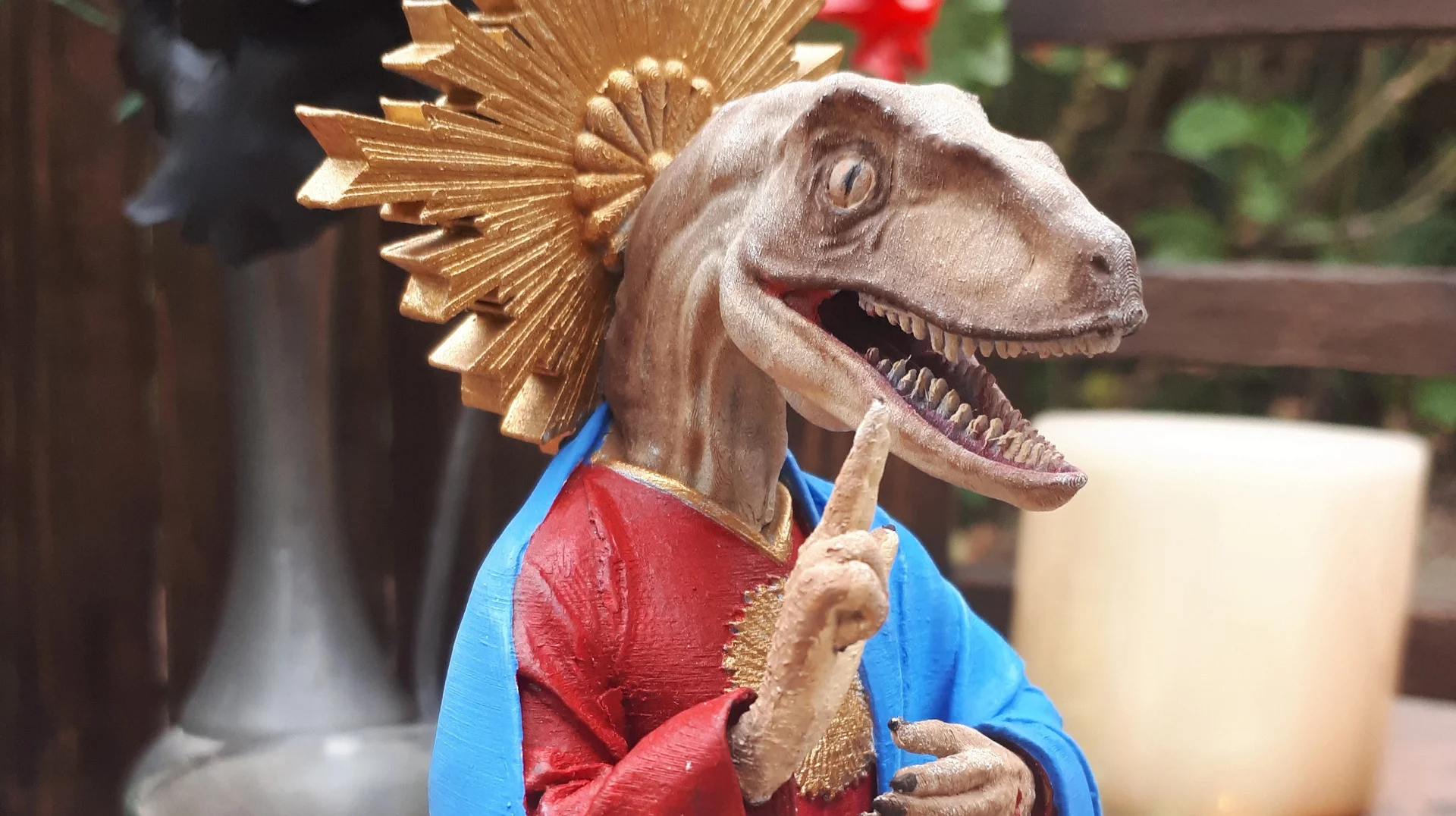 3D-printed Raptor Jesus figurine with golden halo and blue and red robes raising a clawed hand in blessing