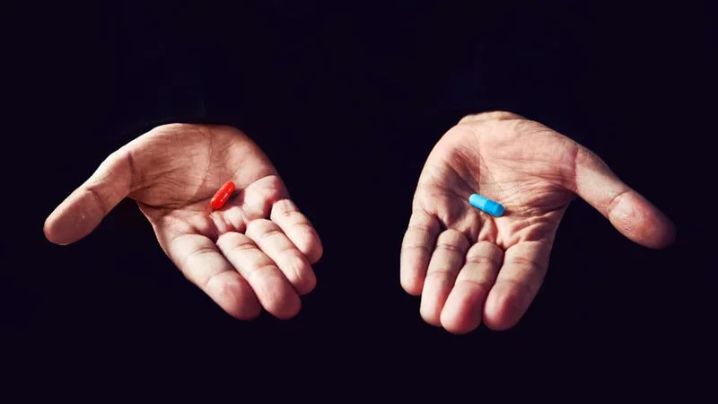 Red Pill — Two open palms extended against a dark black background with a single red capsule in the left hand and a single blue capsule in the right hand.