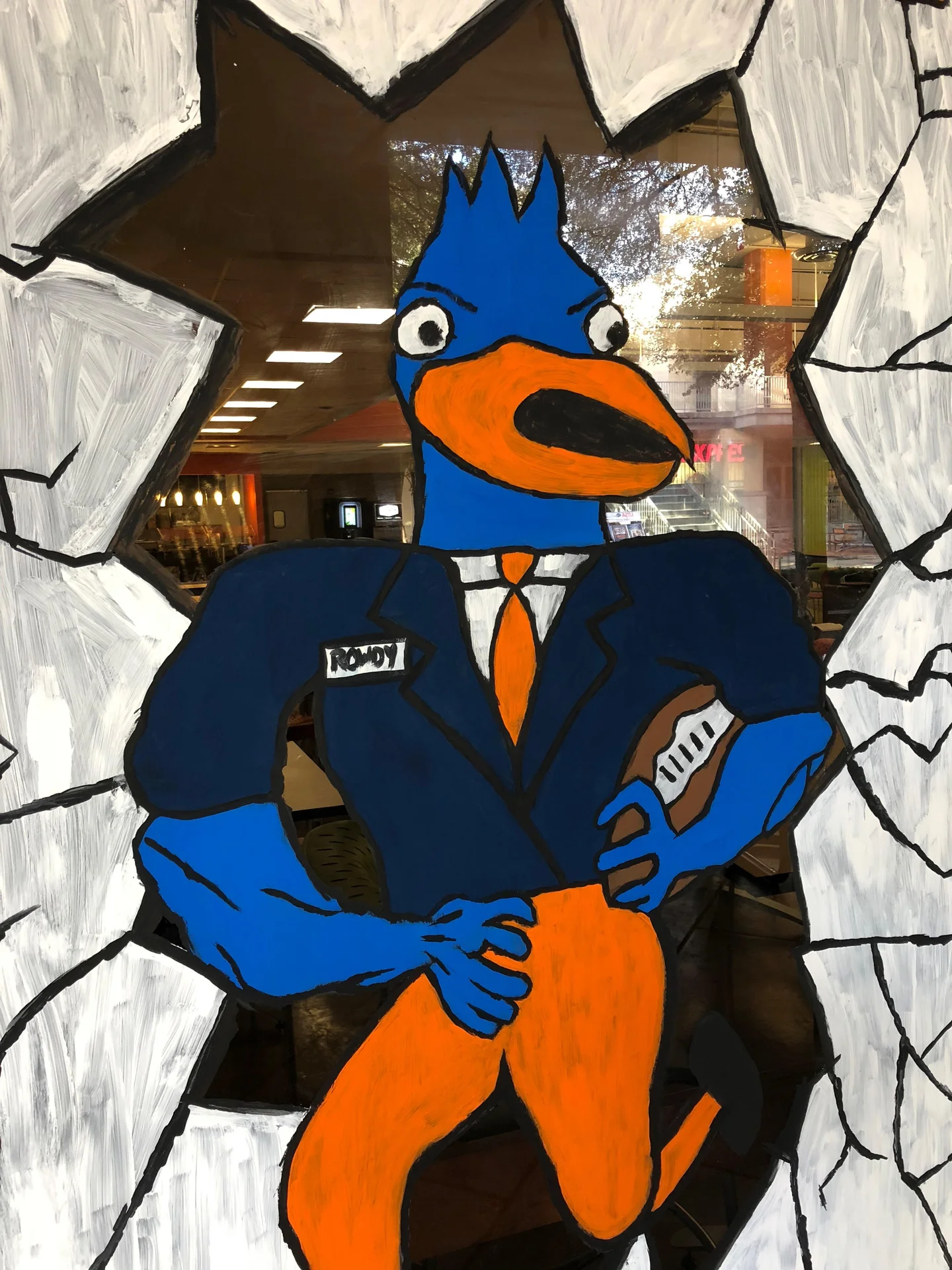 Retarded Rowdy — Amateurishly painted window mural of a blue-and-orange roadrunner mascot in a suit holding a football, with a 'ROWDY' name tag and painted