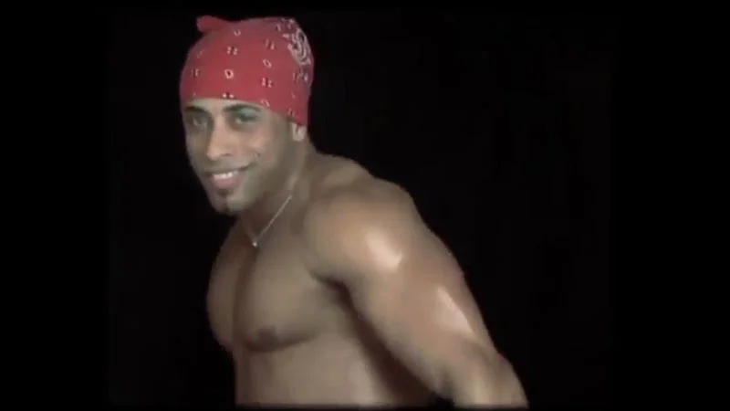 Ricardo Milos — Shirtless man in red bandana smiling against black background