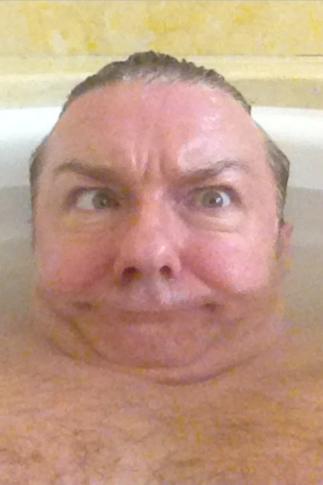 Ricky Gervais making a cross-eyed silly face in the bathtub.