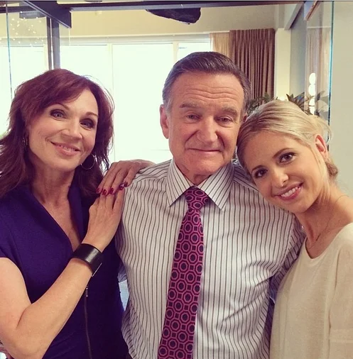 Robin Williams smiling in a group photo with two women, one on each side