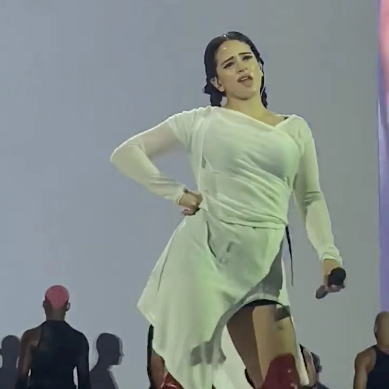 Rosalía Chewing Gum — Close-up of Rosalía on stage making a chewing-gum facial expression in a white dress