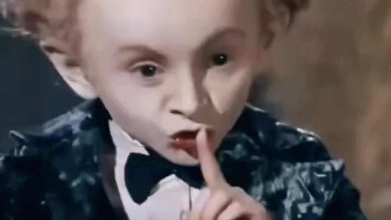 AI-generated Rumpelstiltskin gnome character with curly red hair in a dark jacket, holding finger to lips in a shushing gesture