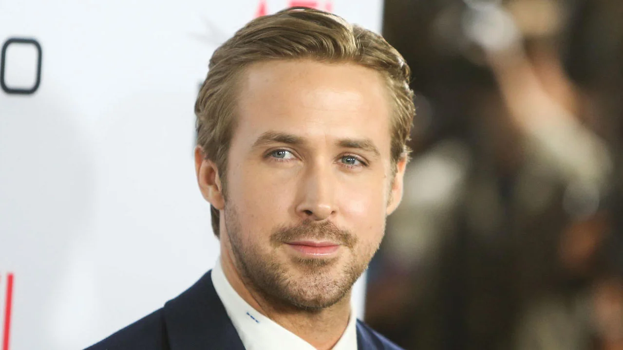 Ryan Gosling smiling on a red carpet in a navy blue suit