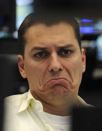 Sad Guys On Trading Floors — A striking close-up photograph of male trader with face contorted into intensely exaggerated sad frown with trading monitors