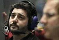 Sad Guys On Trading Floors — A bearded man wearing large noise-canceling headphones gazing forward with sad contemplative expression with blurred person in