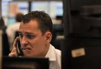 Sad Guys On Trading Floors — A male trader in white dress shirt pressing phone to ear while staring at monitors with visibly anxious and strained expression.