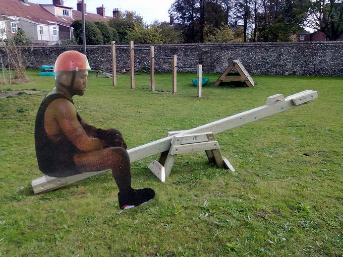 Sad Kanye West photoshopped sitting alone on a wooden seesaw in an empty playground