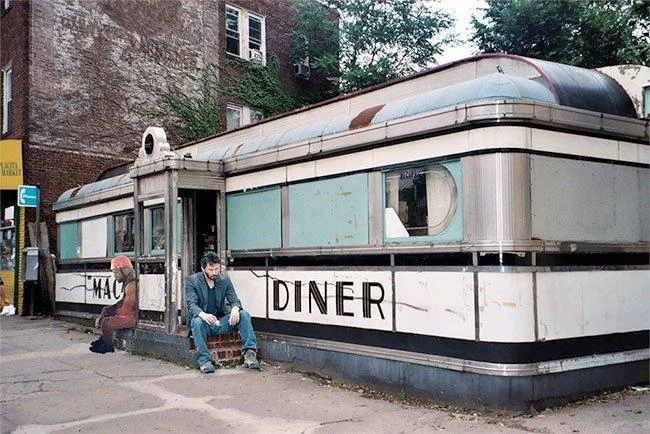 Sad Kanye photoshopped sitting outside a vintage diner beside a lone man