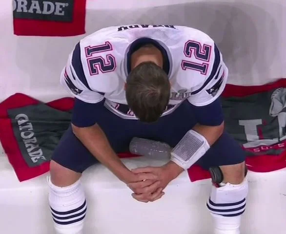 Sad Tom Brady — Tom Brady in Patriots #12 jersey sitting on bench with head down between his knees