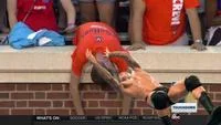 A wider ESPN broadcast angle capturing Sad Virginia Fan in orange UVA shirt against brick wall with Notre Dame 32 score and additional fans in background.