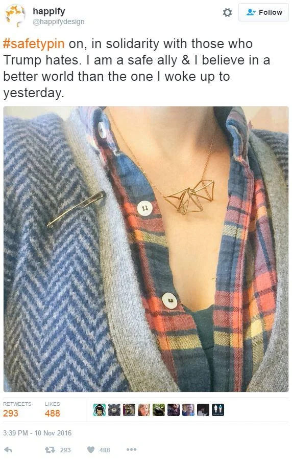 #SafetyPin — Safety pin on a herringbone coat lapel worn by a person with a plaid shirt and geometric necklace