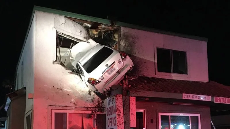 Santa Ana Second Floor Car Crash — Nighttime news photograph showing white sedan fully embedded in second-floor wall of dental office building with car rear