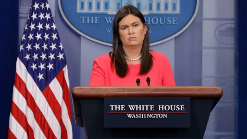Sarah Huckabee Sanders behind White House press briefing podium in coral dress