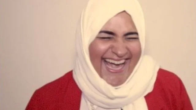 saudis — A clean headshot portrait of smiling person wearing white hijab and red top against neutral beige background with professional lighting.