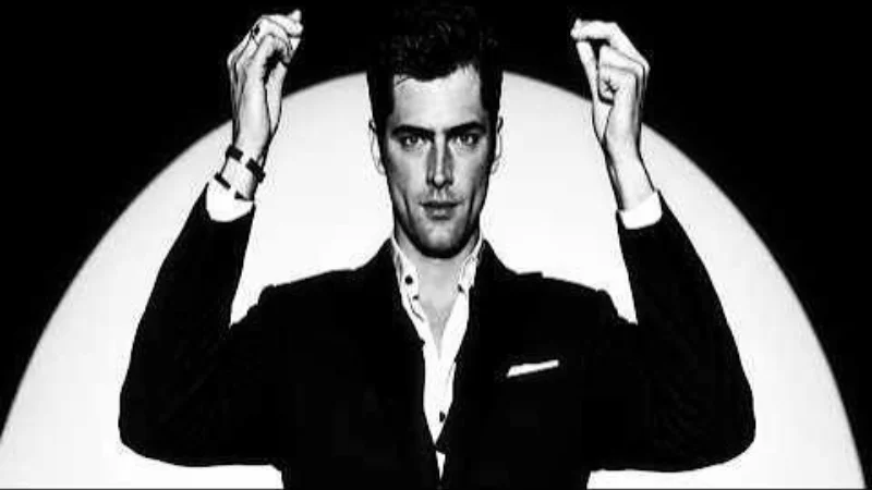 Sean O'Pry Edit — Black-and-white photo of model Sean O'Pry in a dark blazer, hands raised beside his head under a spotlight.