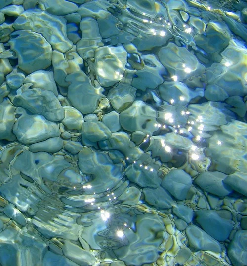 Seapunk — Sunlight sparkles on rippling water over pebbles