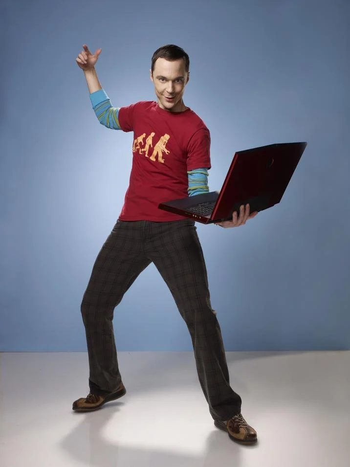 Sheldon Holding a Laptop — Full body shot of Sheldon Cooper in a red shirt posing with raised arm and holding an open laptop